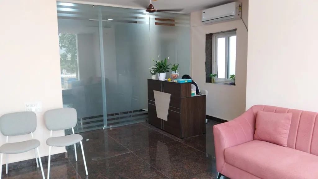 Reception and waiting area at Cura Femina with a dark wood desk, pink sofa, grey chairs, frosted glass partition, and polished dark floor.